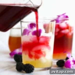 A stream of vibrant, ruby-red hibiscus tea being poured into a clear glass, creating a beautiful visual as it mixes with a lighter liquid below. This image captures the essence of preparing a Hibiscus Arnold Palmer.