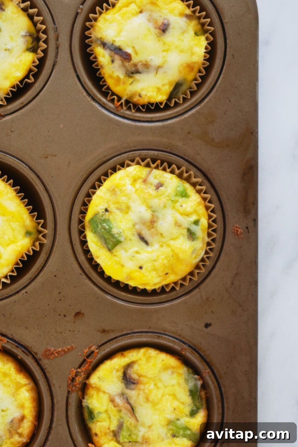 Enjoy these perfectly baked asparagus and mushroom egg cups, ready in under 30 minutes with 4g protein. A cluster of golden-brown baked egg cups, fresh out of the oven, highlighting their perfect shape and appealing texture.