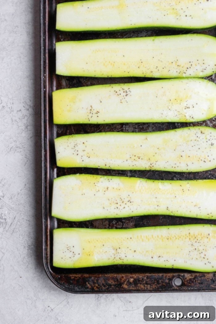 Fresh zucchini, glistening with a drizzle of olive oil, neatly arranged on a baking sheet before grilling.