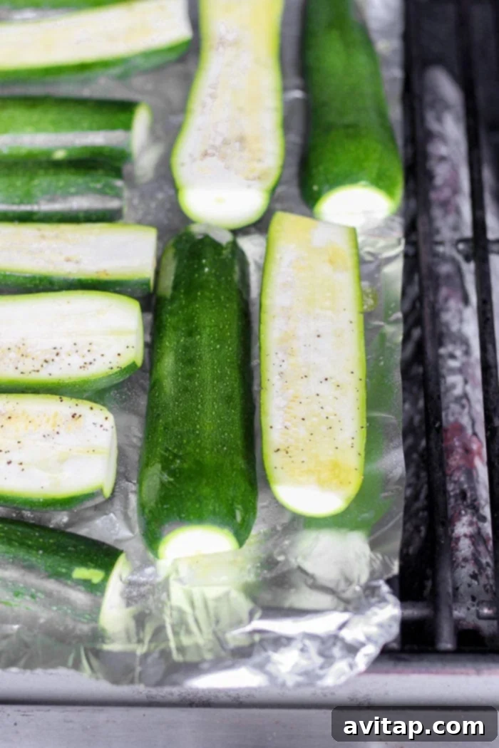 Zucchini halves sizzling on a hot grill, showing developing char marks.