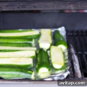 Grilled zucchini cooking on a foil sheet over direct flame, showing initial charring.