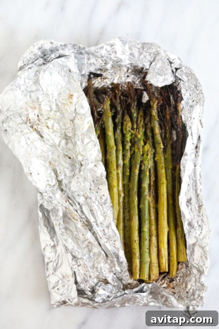Grilled asparagus spears emerging from a foil pack, glistening with olive oil and seasoning, ready to be served.