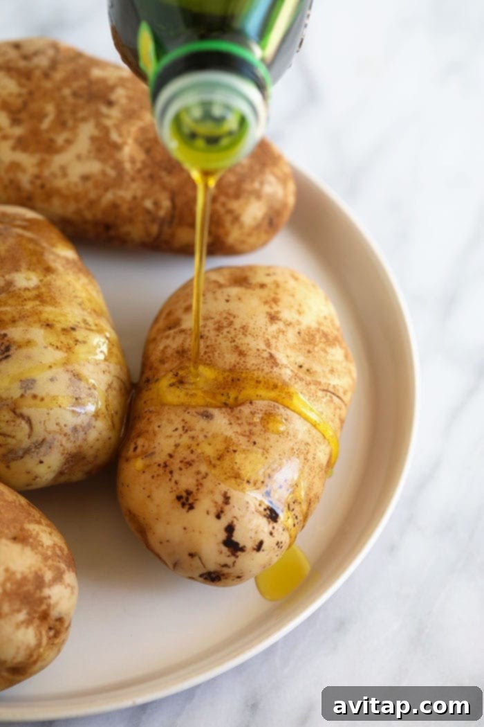 Foil-Wrapped Baked Potatoes 3 Olive oil being drizzled over cleaned and dried potatoes before seasoning and baking.