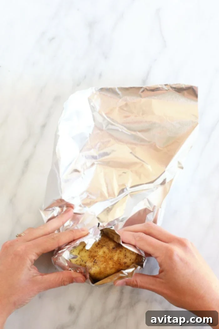 Foil-Wrapped Baked Potatoes 4 Hands demonstrating the process of rolling a potato securely in tin foil, preparing it for baking.