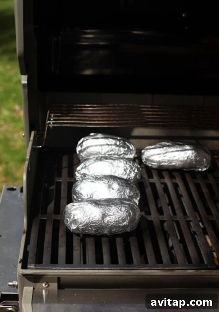 Foil-Wrapped Baked Potatoes 5 Baked potatoes wrapped in foil cooking directly on grill grates, ready for a delicious meal.