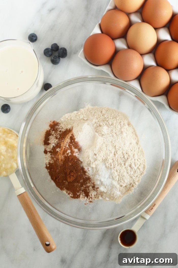 Mixing the perfect banana pancake muffin batter for a consistent, fluffy texture. Banana pancake muffin batter being mixed in a large glass bowl with a whisk.