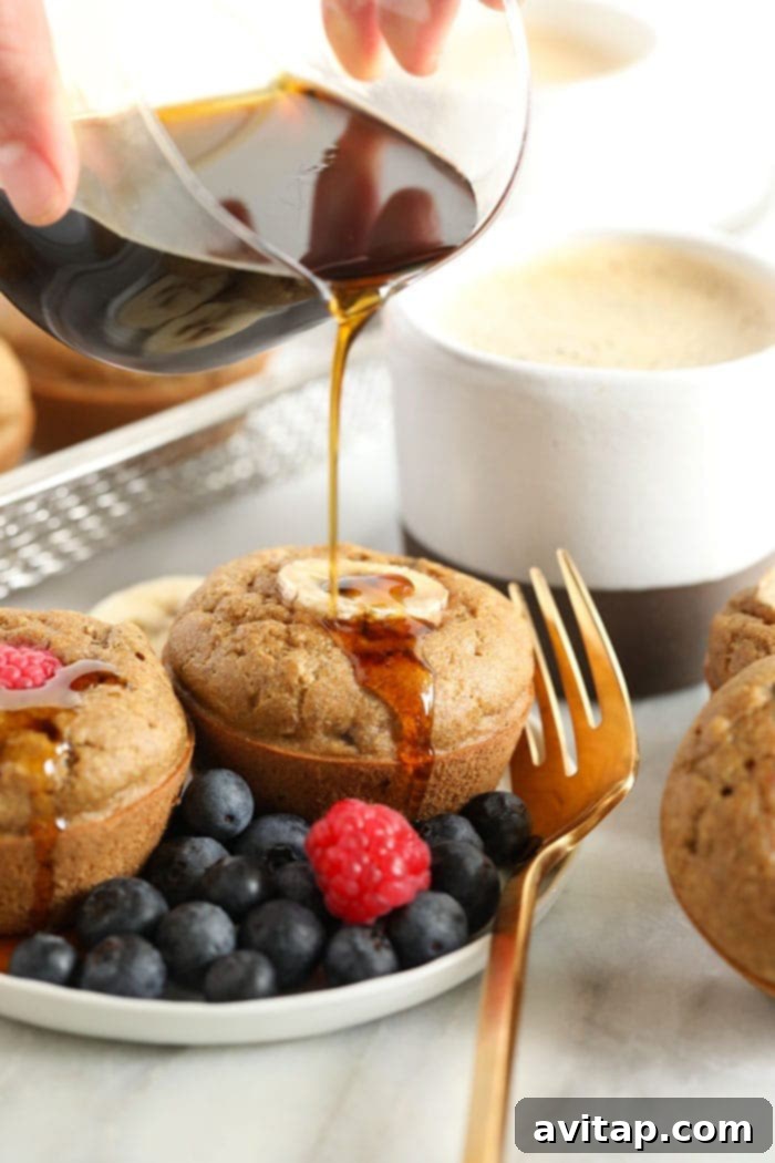 Serving warm Banana Pancake Muffins with a drizzle of maple syrup. Close-up of baked banana pancake muffins being drizzled generously with maple syrup, showcasing their fluffy texture.