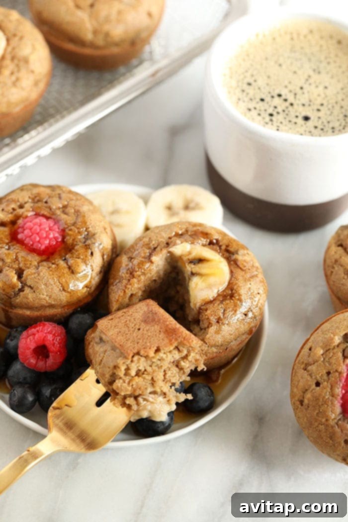 Enjoying your homemade fluffy Banana Pancake Muffins for breakfast. Three banana pancake muffins on a plate, ready to be eaten, showing their golden brown tops and soft interior.