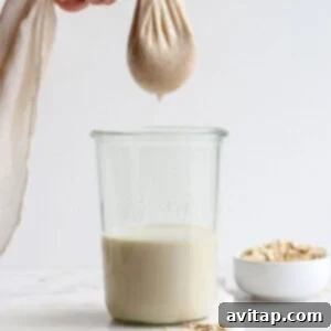 Squeezing oat milk out of cheesecloth into a jar.