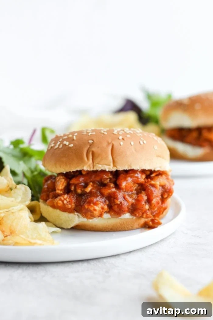 The perfectly savory and sweet Healthy Sloppy Joe Recipe is here! Made with ground chicken and a flavorful sauce packed with clean ingredients, these Sloppy Joes will not disappoint! Healthy sloppy joe on a bun with chips, showcasing a delicious meal