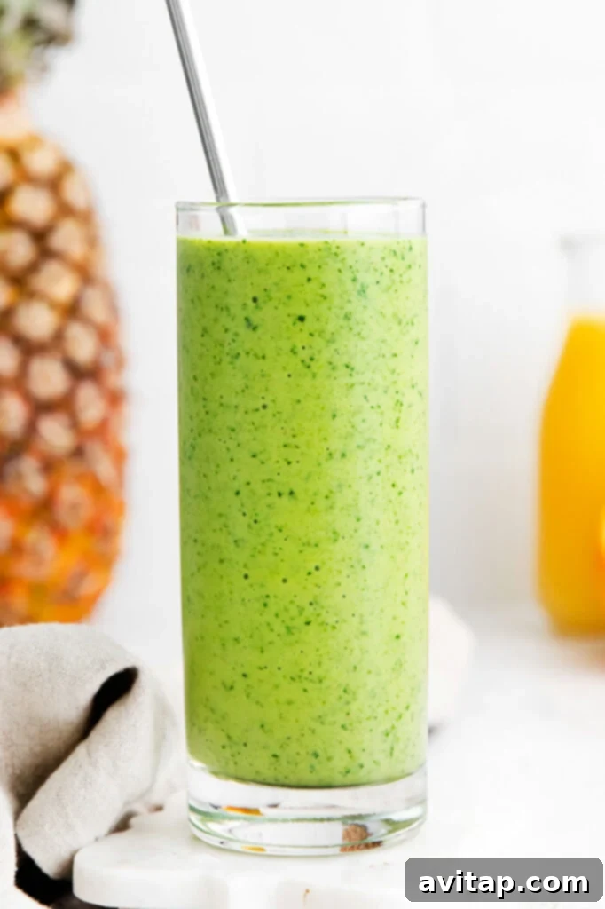 A vibrant green tropical spinach smoothie in a glass, garnished with fresh oranges and pineapple slices, showcasing its refreshing appeal.