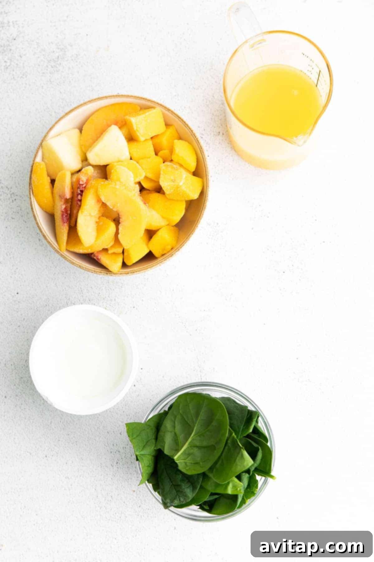Individual ingredients for a tropical spinach smoothie laid out in small bowls: frozen tropical fruit blend, fresh spinach, Greek yogurt, and orange juice, ready for blending.