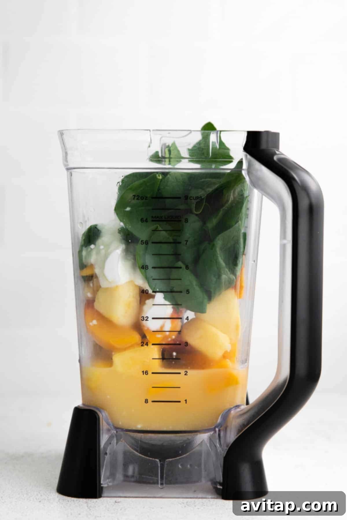 All the vibrant ingredients for the spinach smoothie, including frozen fruit and fresh spinach, placed in a blender carafe, ready to be processed into a creamy drink.