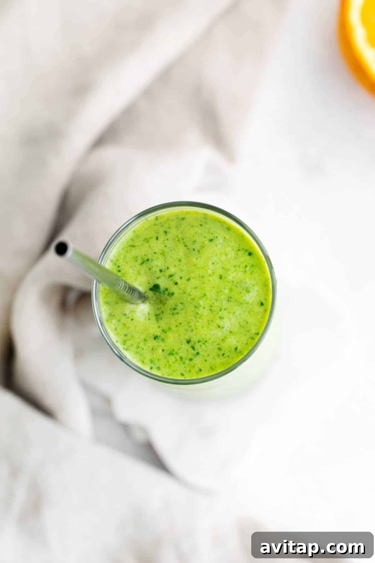 A close-up view of the top of a tropical spinach smoothie in a glass, highlighting its smooth, thick texture and vibrant green color.