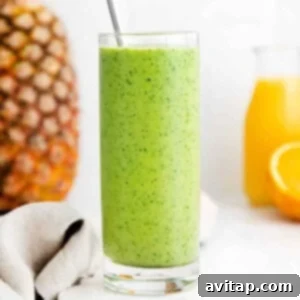 A vibrant green spinach smoothie in a glass with fresh fruit in the background, ready to be enjoyed.