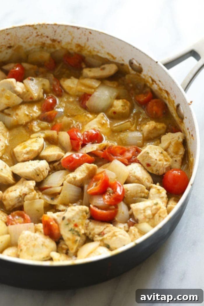 Pesto chicken pasta being mixed in a large skillet pan, showcasing the rich green sauce and colorful ingredients.