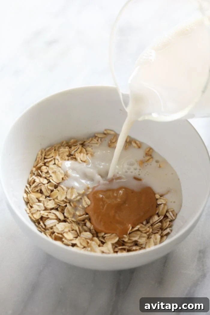 Pouring almond milk into a bowl of dry rolled oats, illustrating the liquid addition step for microwave oatmeal.