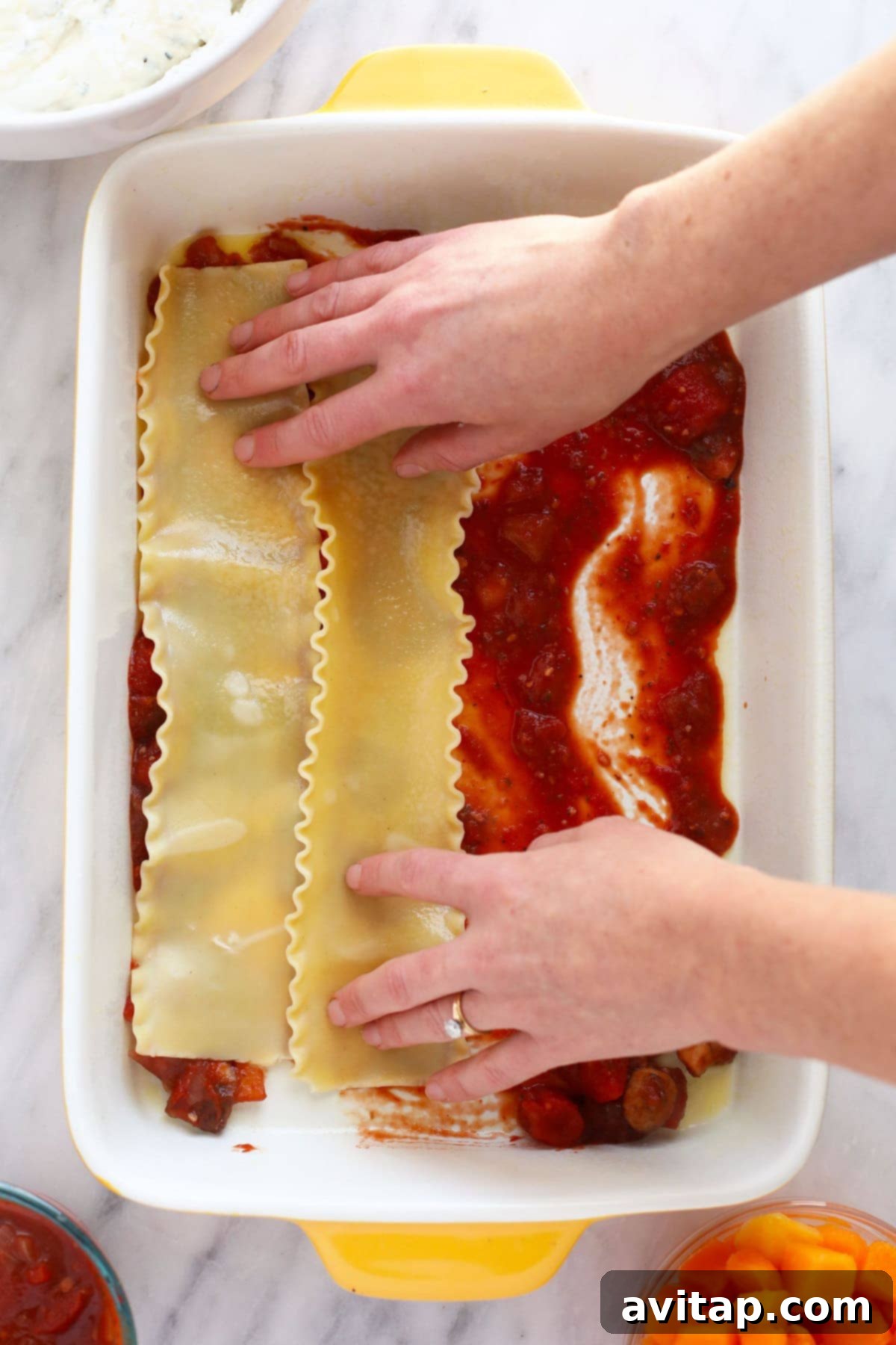 Hands carefully placing lasagna noodles into a 9x13 casserole dish, forming the first layer.