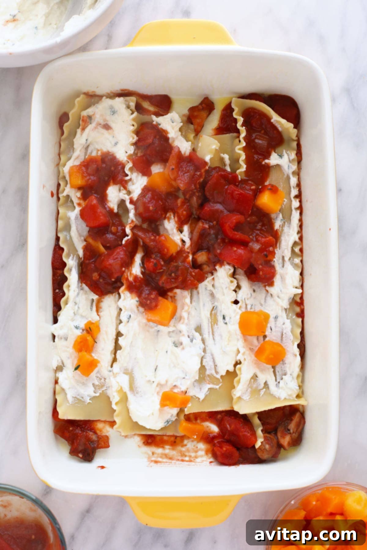 The process of assembling butternut squash lasagna layers in a 9x13 pan, showing the rich sauce, creamy cheese, and noodles.