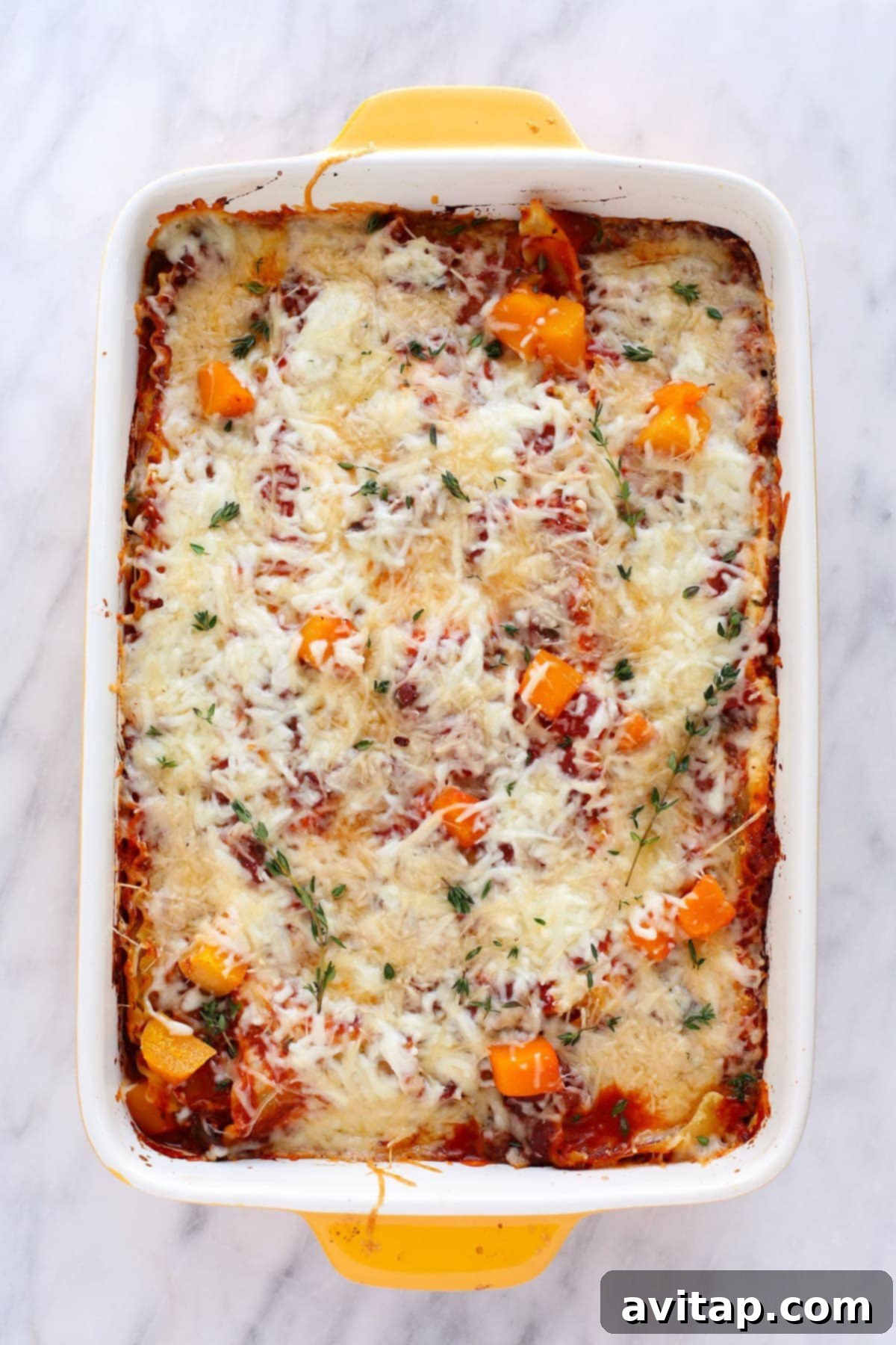 A freshly baked butternut squash lasagna, golden brown and garnished with fresh thyme, cooling in its pan.