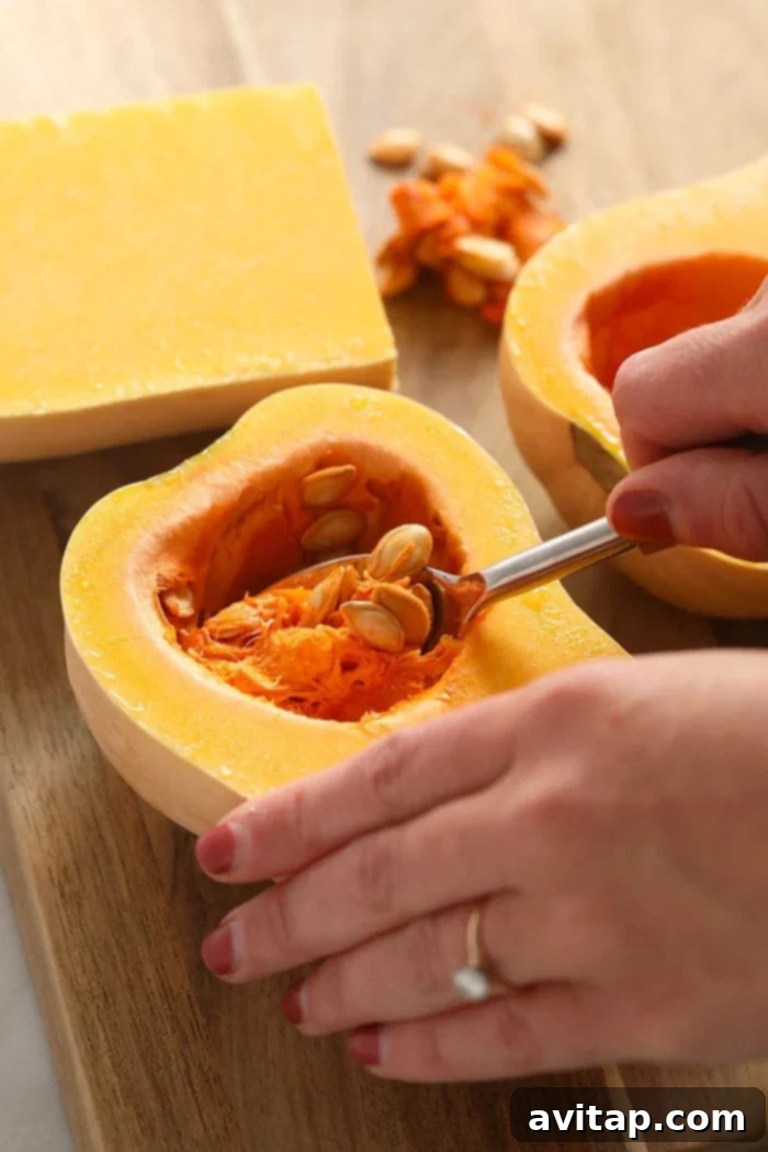 Instant Pot Butternut Squash Recipe 3 A person scooping the innards and seeds out of a halved butternut squash.