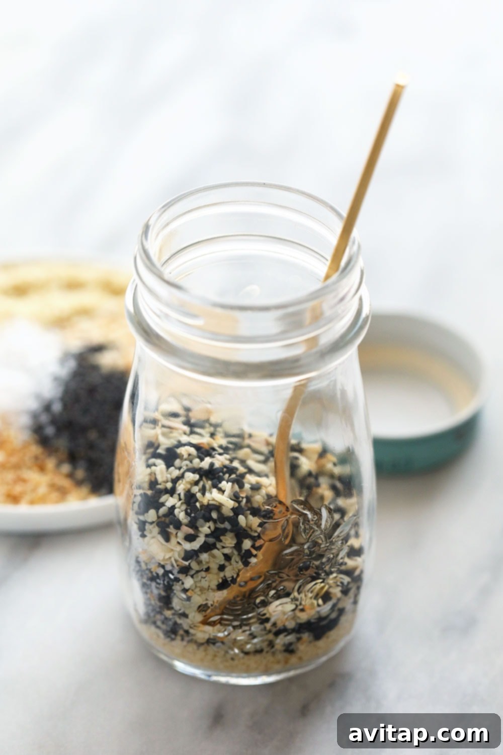 Everything Bagel Seasoning in a small glass jar with a scoop.