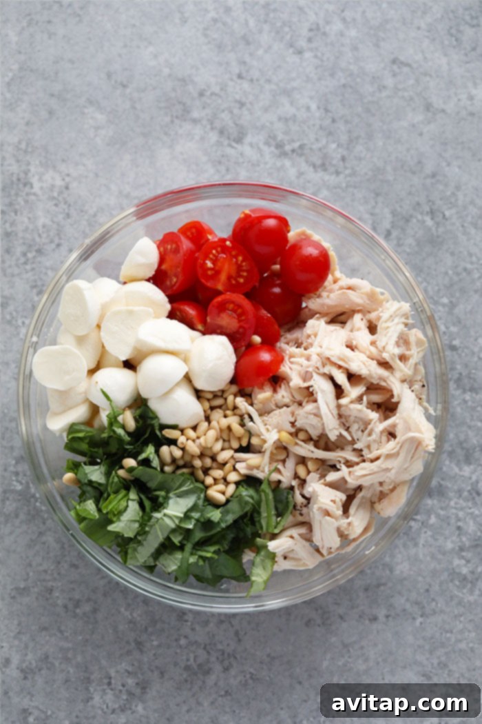 Fresh Ingredients for Creamy Pesto Chicken Salad A selection of fresh ingredients for pesto chicken salad, including cherry tomatoes, mozzarella balls, pine nuts, and fresh basil, artfully arranged in a bowl.