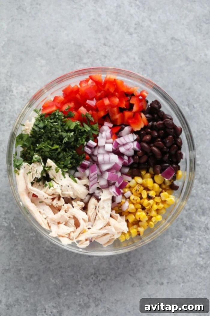A glass bowl filled with the colorful ingredients for Southwest Chicken Salad before mixing, highlighting the fresh vegetables and shredded chicken.