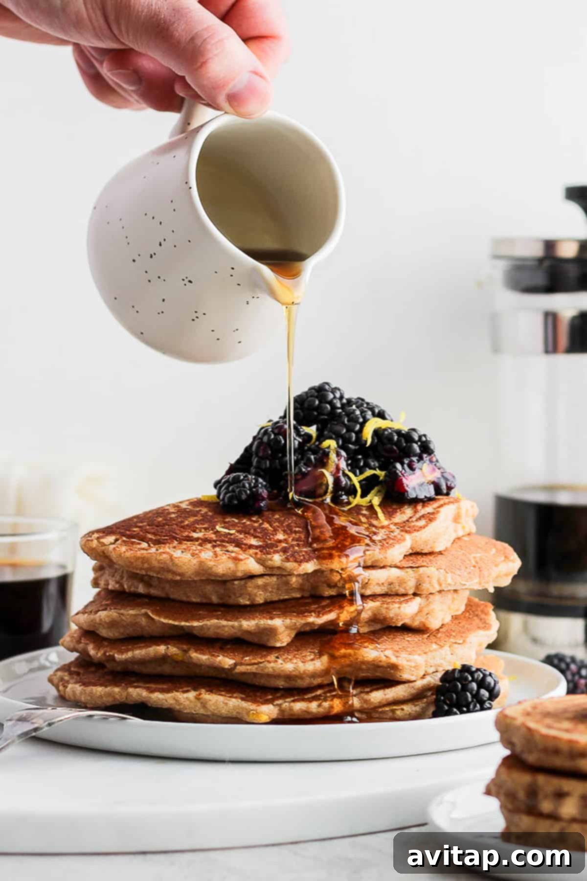 Freshly stacked lemon ricotta pancakes drizzled with syrup and berries on a white plate.
