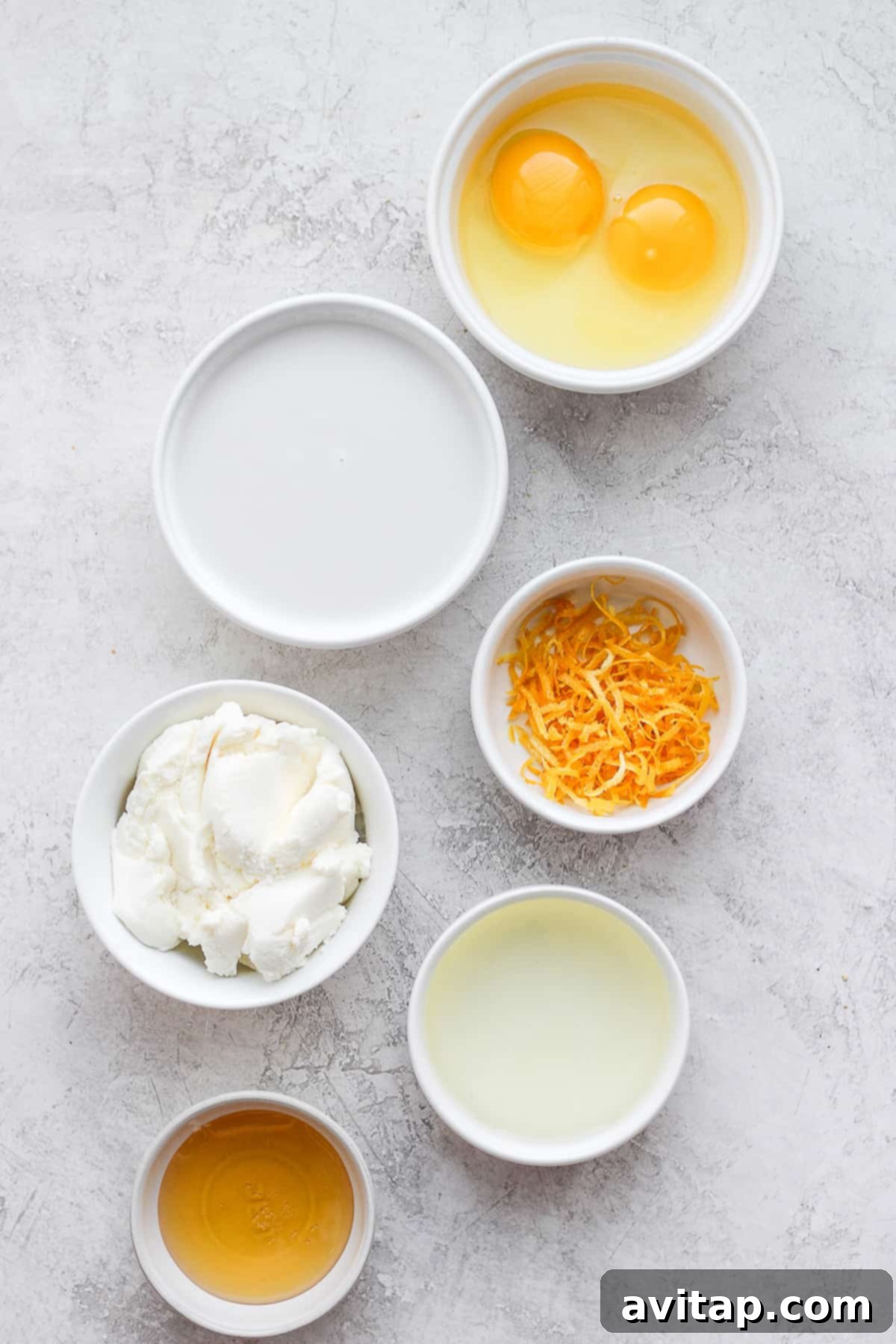 Assortment of fresh ingredients including lemons, ricotta cheese, flour, eggs, and honey laid out on a kitchen countertop.