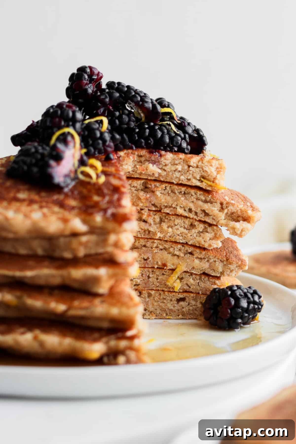 A tall stack of fluffy lemon ricotta pancakes garnished with fresh berries and powdered sugar, ready to be served.
