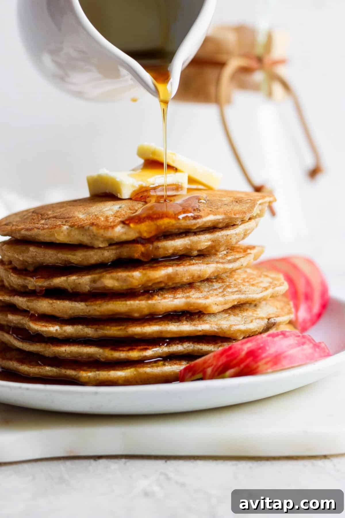 A tall stack of fluffy Apple Pancakes drizzled with golden syrup, inviting you to indulge in a perfect fall breakfast.