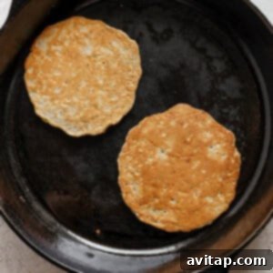Two golden brown pancakes cooking in a cast iron skillet, ready to be flipped.