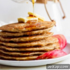 A stack of finished apple pancakes with syrup being generously poured over them.