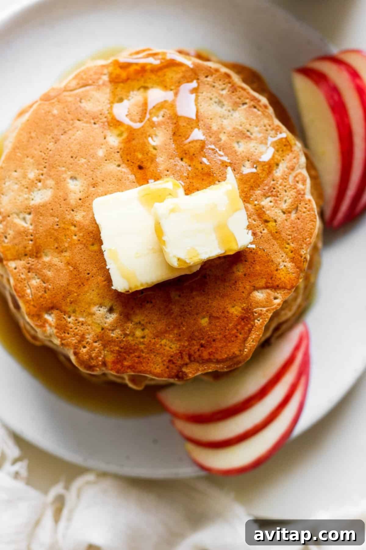 A plate of warm apple pancakes garnished with a pat of butter and fresh apple slices, ready to be enjoyed.