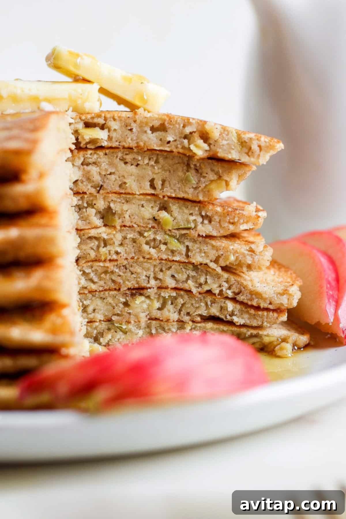A beautifully arranged plate featuring a stack of apple pancakes, garnished with fresh apple slices and a sprig of mint.
