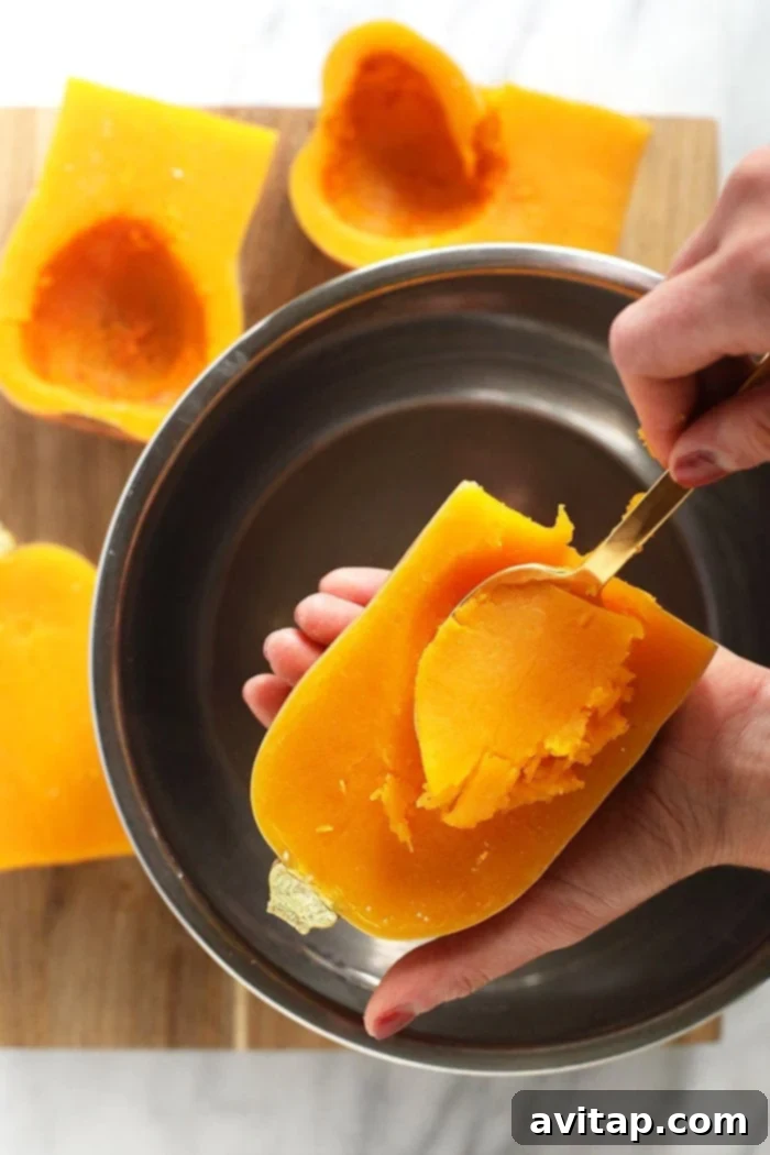A spoon scooping the soft, cooked flesh from a roasted butternut squash half, showcasing its tender texture