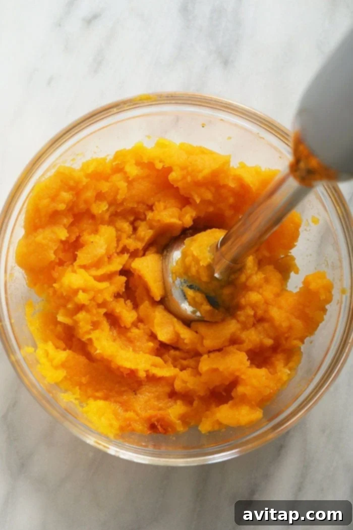 An immersion blender actively pureeing cooked butternut squash in a large bowl, creating a smooth, creamy texture