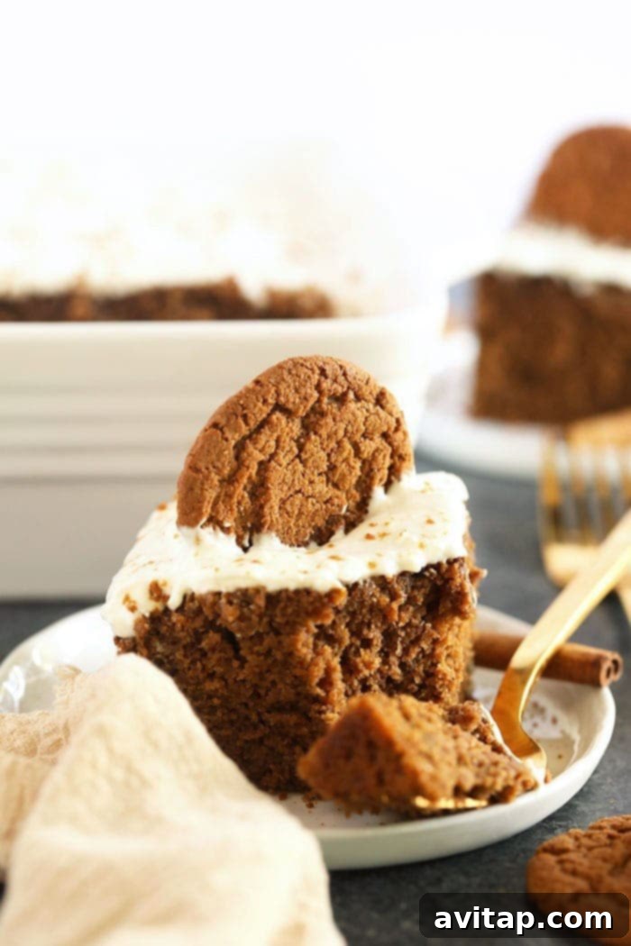 A perfectly sliced piece of classic gingerbread, generously topped with creamy white lightened-up cream cheese frosting, resting on a white plate, ready to be enjoyed as a festive holiday dessert.