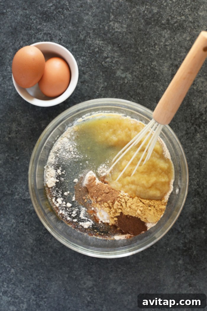A collection of fresh, high-quality ingredients for gingerbread baking, including flour, spices, applesauce, molasses, eggs, and brown sugar, neatly arranged on a counter before mixing.
