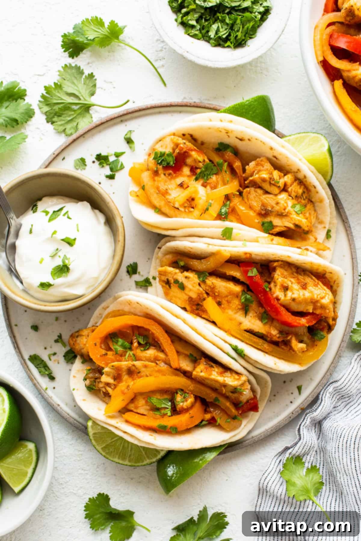 Chicken fajita tacos on a plate with limes and sour cream.