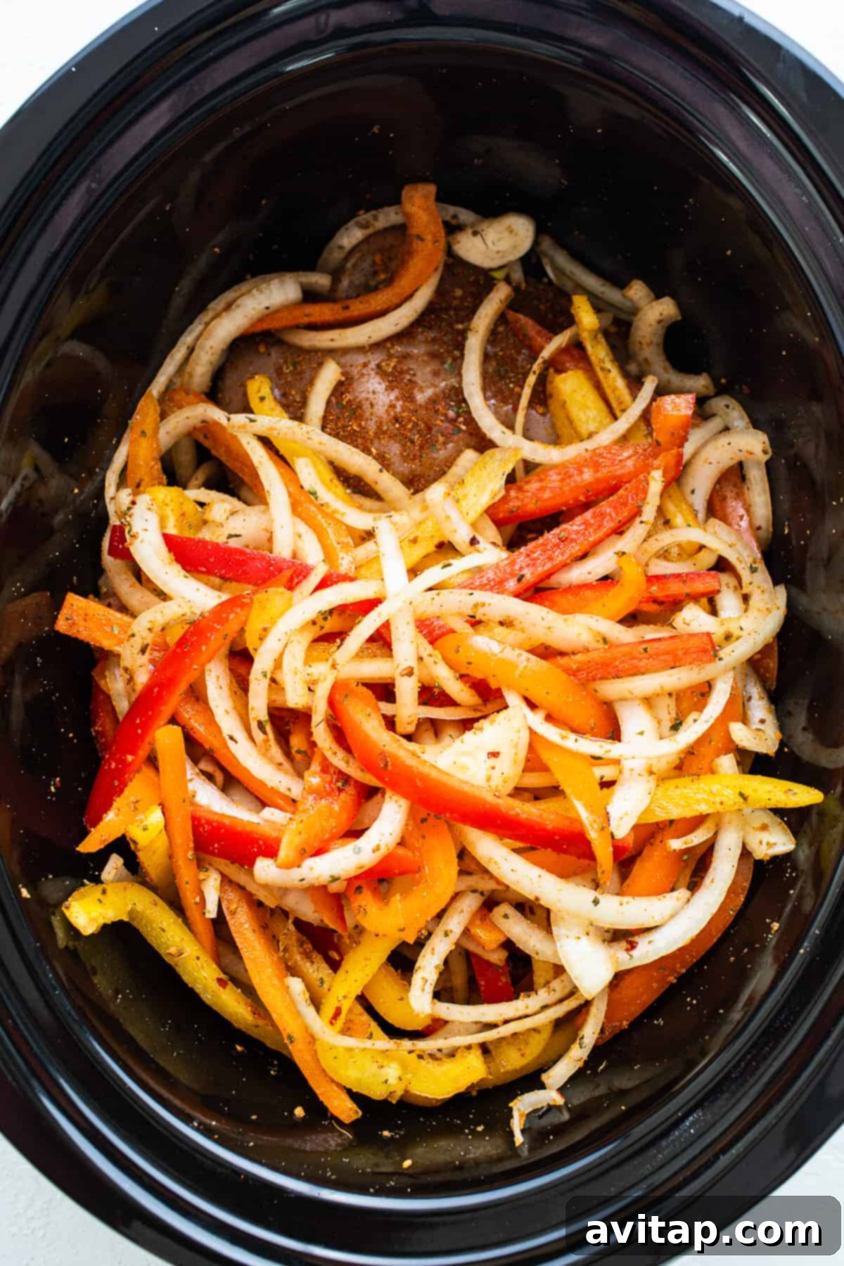 A crock pot filled with peppers and onions.