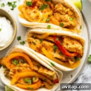 Three chicken tacos with peppers and sour cream on a plate.