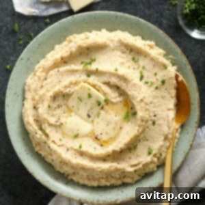 Cauliflower mashed potatoes served in a white bowl, garnished with butter, pepper, and herbs.