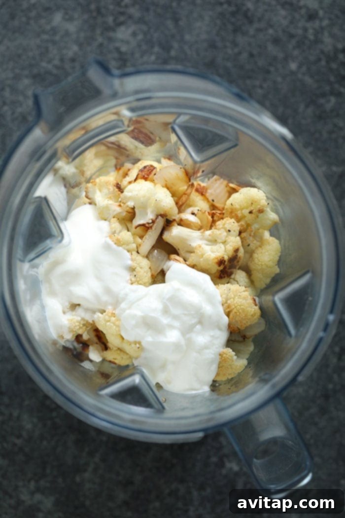 All the roasted ingredients for cauliflower mash, including cauliflower, garlic, and onions, along with dairy and broth, loaded into a high-speed blender.