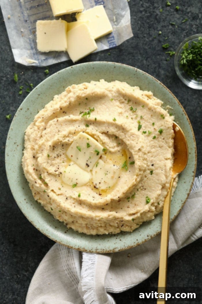 A bowl of creamy cauliflower mashed potatoes, topped with melted butter, fresh parsley, and cracked black pepper.