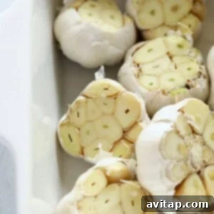 Multiple fresh garlic bulbs with their tops sliced, arranged cut-side up in a baking dish, ready for seasoning.