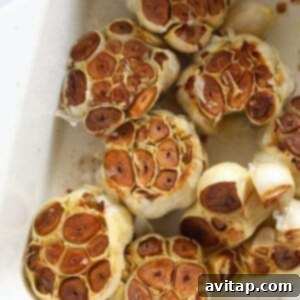 Several garlic bulbs, glistening with olive oil, roasting in a baking dish in the oven, showing early signs of browning.