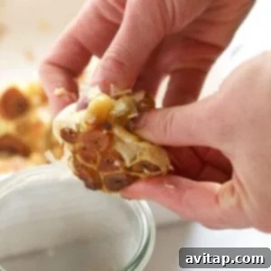 A hand gently squeezing a roasted garlic bulb, with the soft, caramelized cloves easily emerging from their skins.