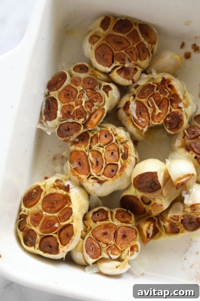 A full baking dish filled with multiple roasted garlic bulbs, beautifully golden and tender, fresh out of the oven.